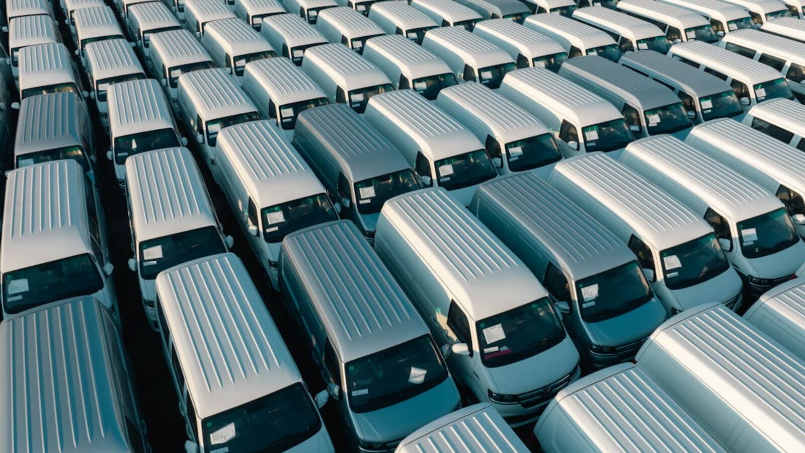 Кейс: продажа автомобиля в лизинге в Санкт-Петербурге — Aerial shot of multiple white vans parked in orderly rows in a lot under daylight.