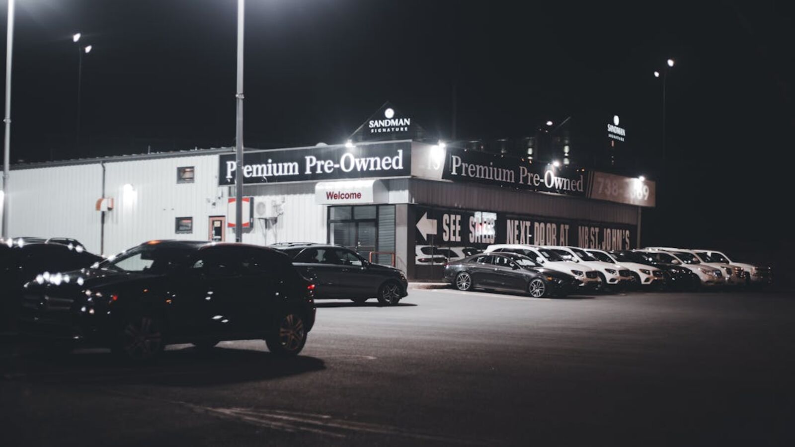 Кейс: продажа автомобиля с большим пробегом в Санкт-Петербурге — Illuminated car dealership lot showcasing premium pre-owned vehicles at night.