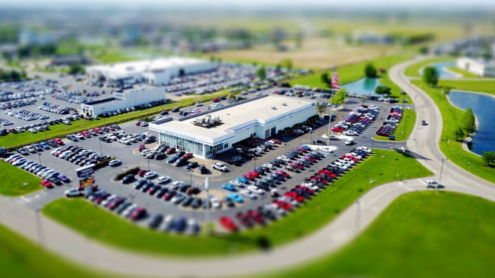 Выкуп автомобилей с пробегом в Санкт-Петербурге — Aerial high-angle view of a bustling car dealership surrounded by parked cars in a green landscape.
