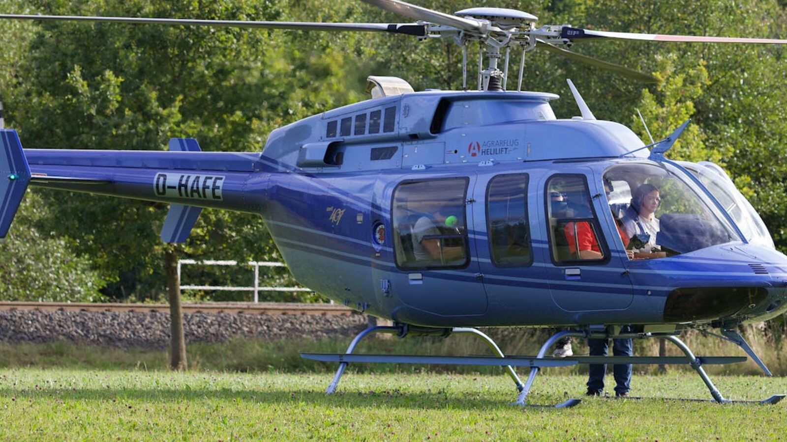 Кейс: продажа частного вертолёта в Санкт-Петербурге — A blue helicopter parked on a green field with a person nearby, outdoors.