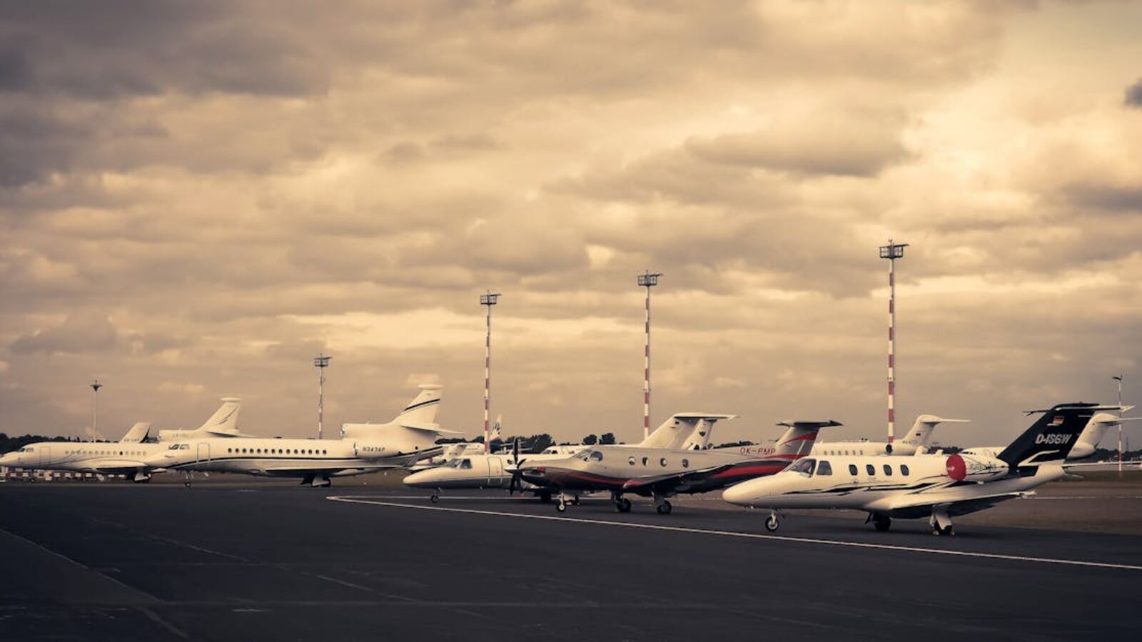 Выкуп бизнес-джетов в Санкт-Петербурге — Line of private jets parked on the tarmac under a dramatic cloudy sky, showcasing aviation and travel.