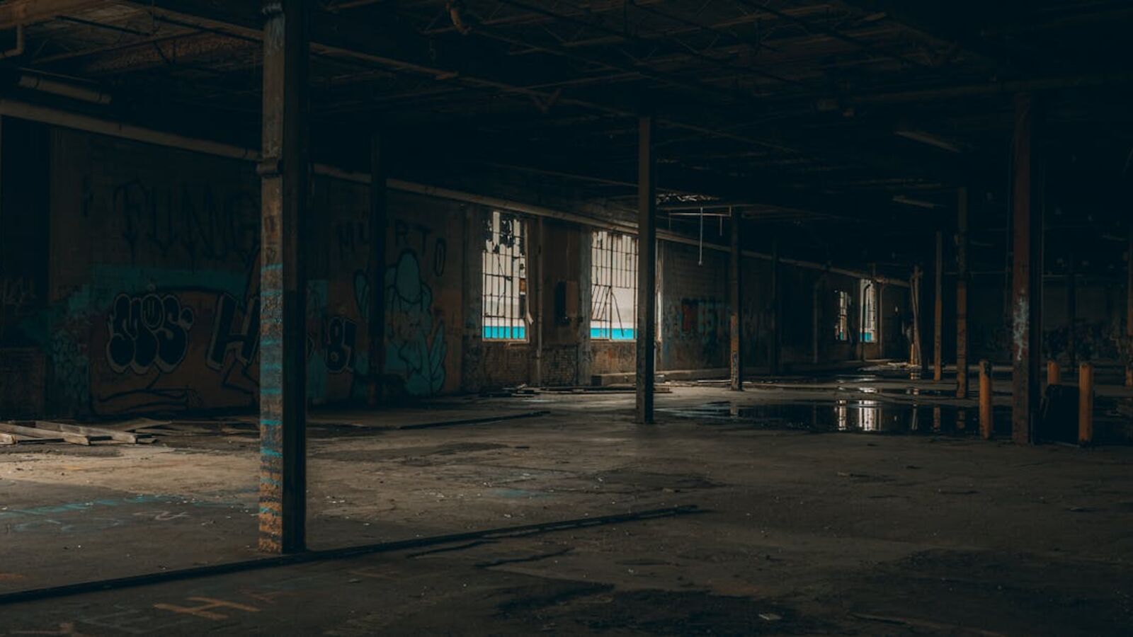 Кейс: продажа готового арендного бизнеса в Санкт-Петербурге — Dark and moody interior of a large abandoned warehouse with graffiti walls and broken windows.