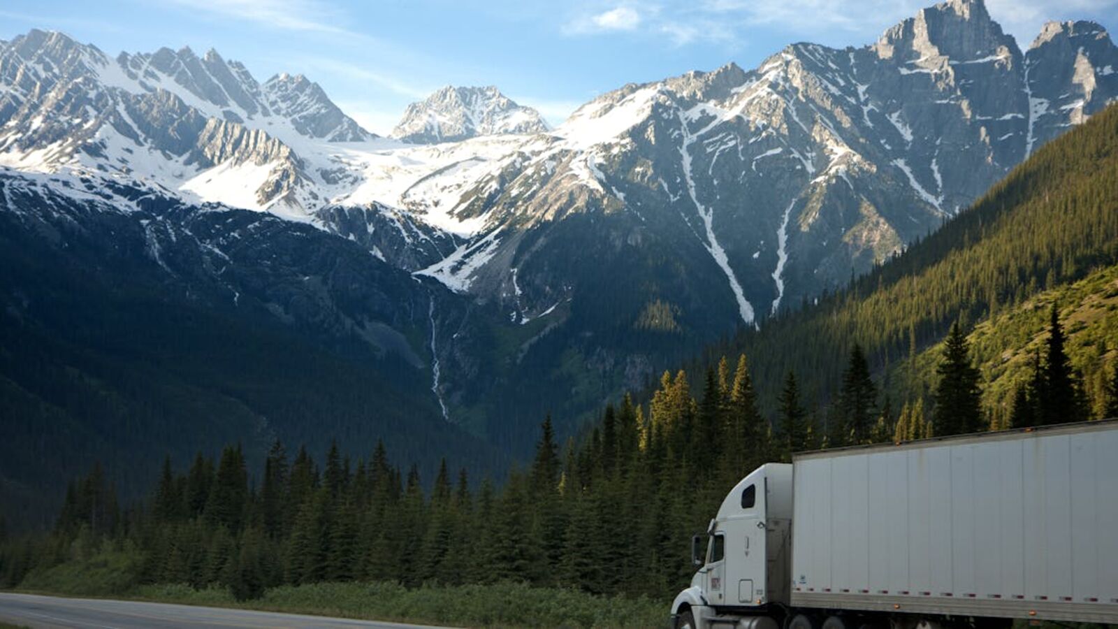 Кейс: продажа рефрижератора как коммерческого актива в Санкт-Петербурге — A semi-truck travels along a highway with snow-capped mountains in the background.