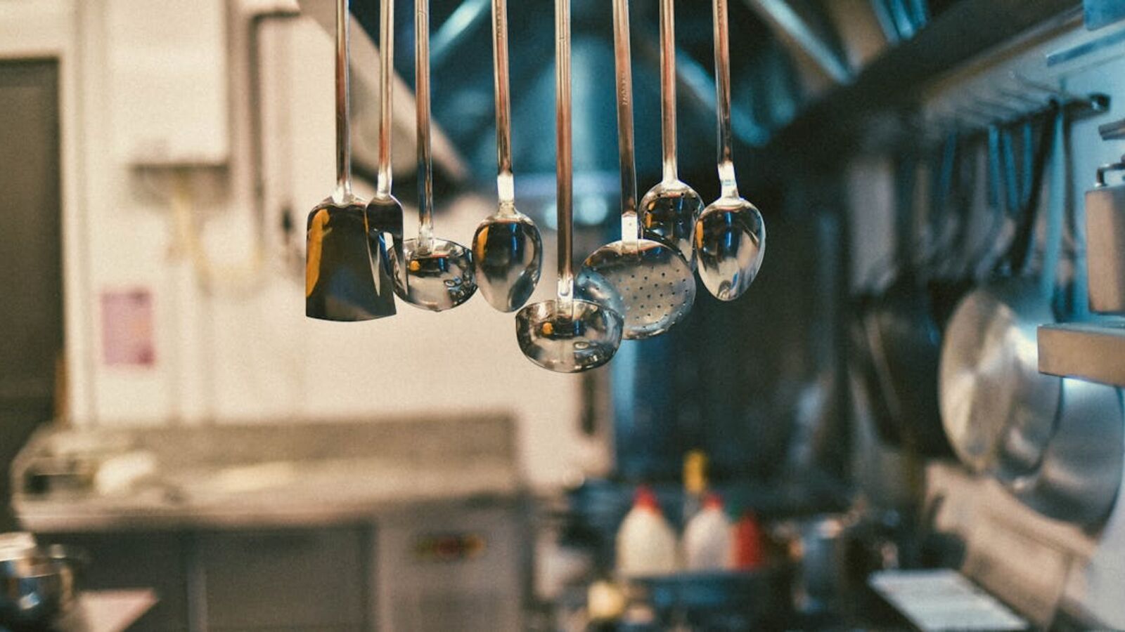 Кейс: продажа оборудования пищевого цеха при смене профиля в Санкт-Петербурге — Stainless steel kitchen utensils hanging in a modern kitchen setting with blurred background.