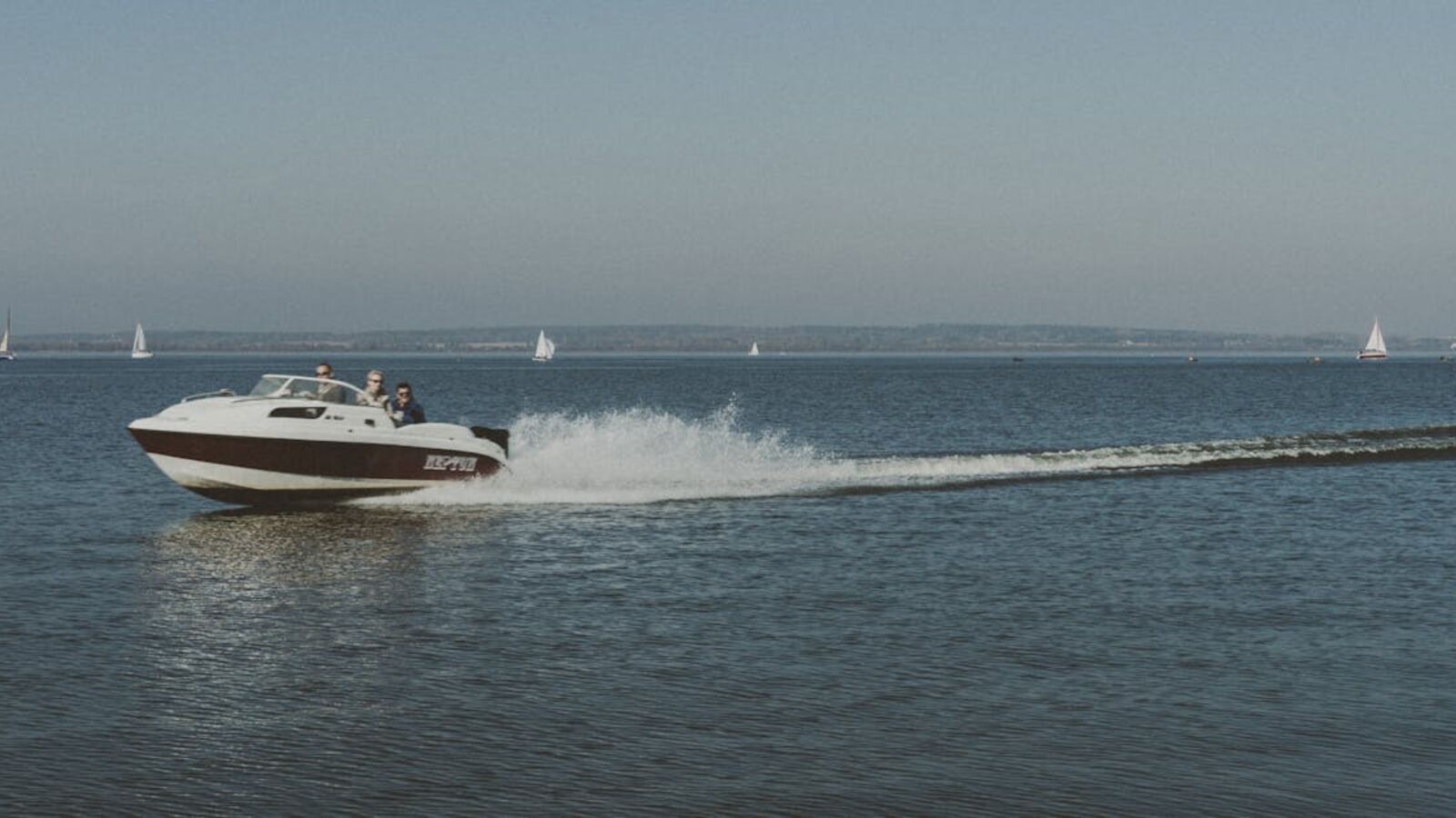 Кейс: продажа лодочного мотора отдельно в Санкт-Петербурге — Motorboat speeding on a clear water body with sailboats in the distance on a sunny day.