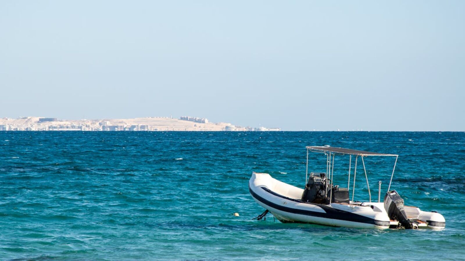 Кейс: продажа RIB-лодки после хранения в Санкт-Петербурге — Inflatable RIB boat moored on clear blue sea with distant cityscape, under bright daylight.